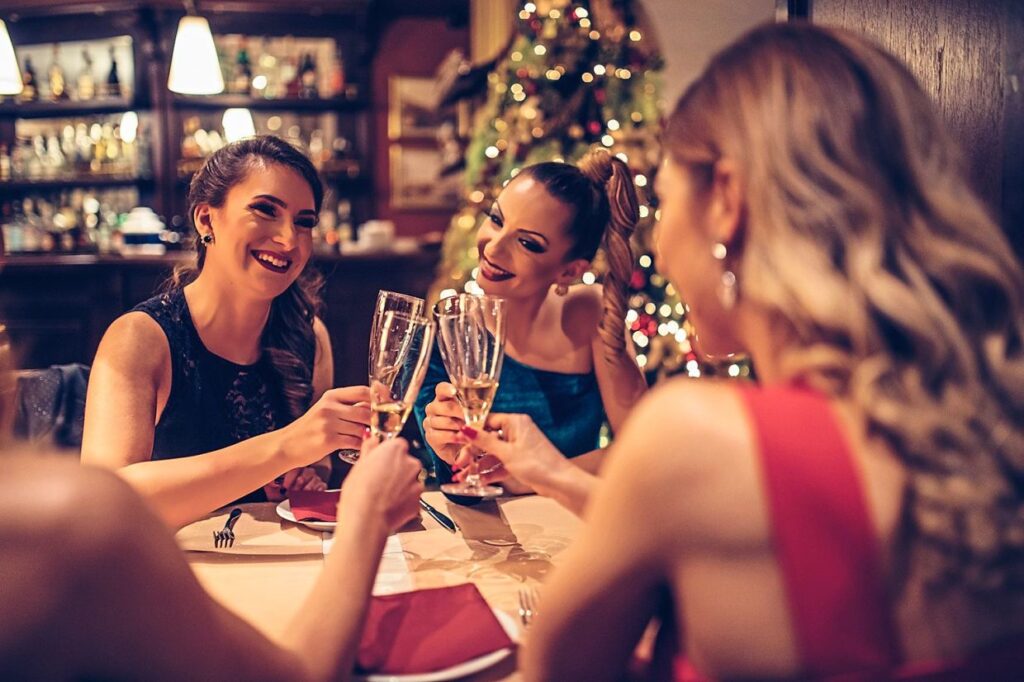 Group of young and beautiful women celebrating Christmas day in a glamorous style, in the Nuthurst Grange restaurant. They are sitting at the table and saying cheers.